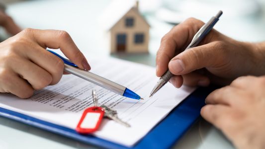 Contract with house keys on it and two hands holding pens 